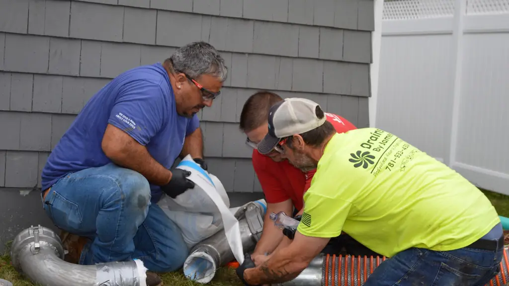 Three Drains By James technicians feeding a white CIPP liner sleeve into a pipe beside a house